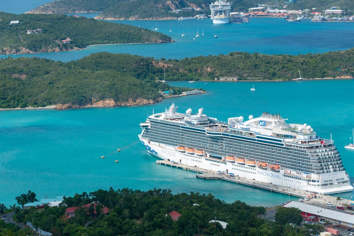 A large cruise ship docked in a turquoise Caribbean bay among green hills