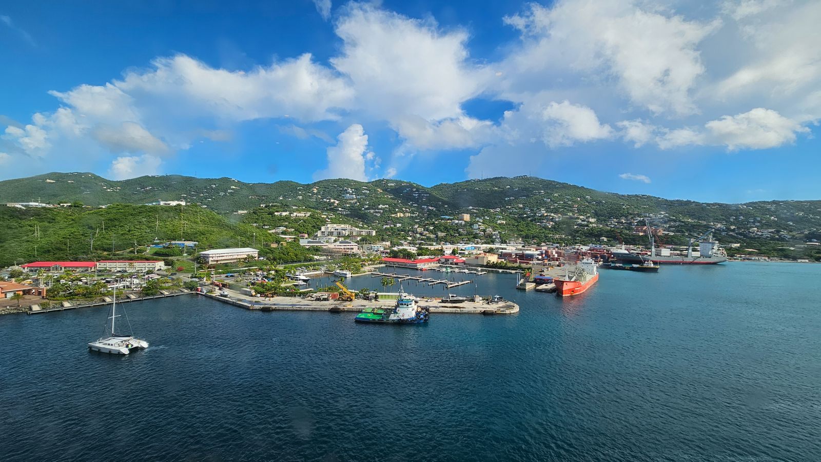 A green Caribbean island harbour under a blue sky with puffy clouds