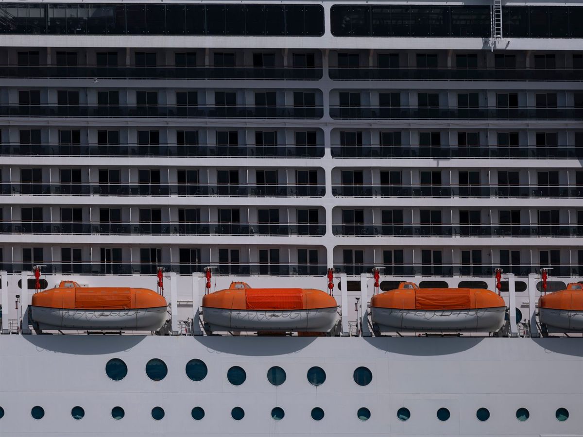 Rows of cabin windows and portholes above orange lifeboats on a cruise ship hull